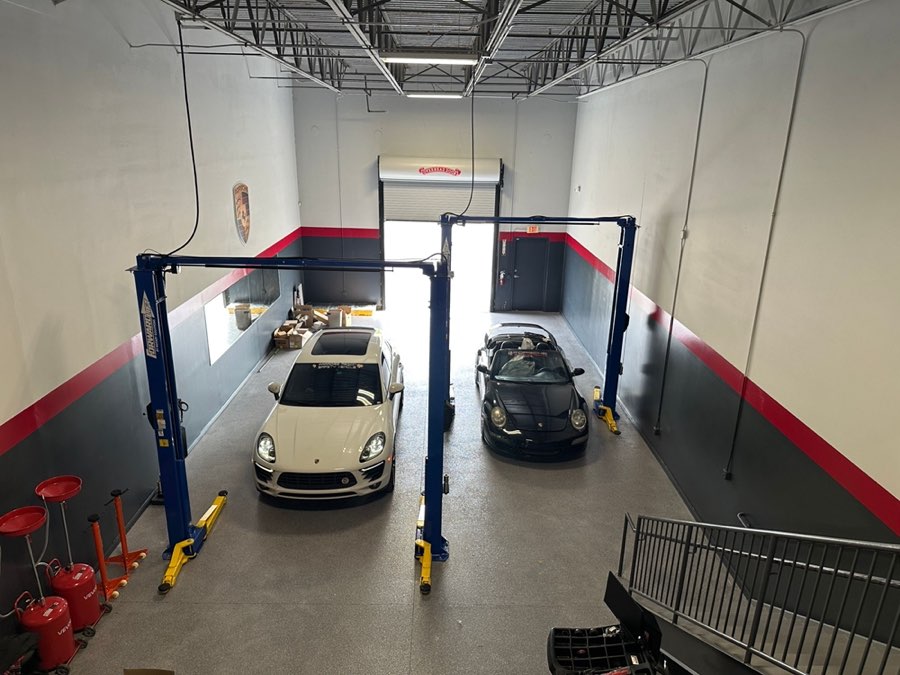 Overhead view of the shop with a white Macan and a black 911 Cabriolet in the lift bays