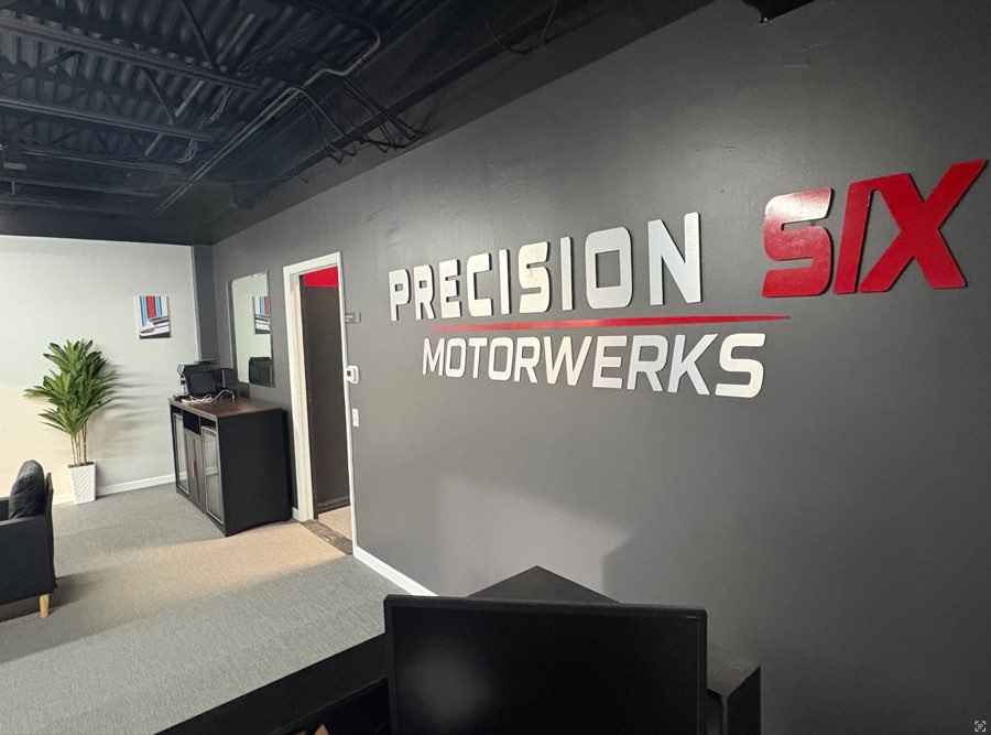 Precision Six Motorwerks sign on the grey lobby wall, beside the coffee bar and waiting area
