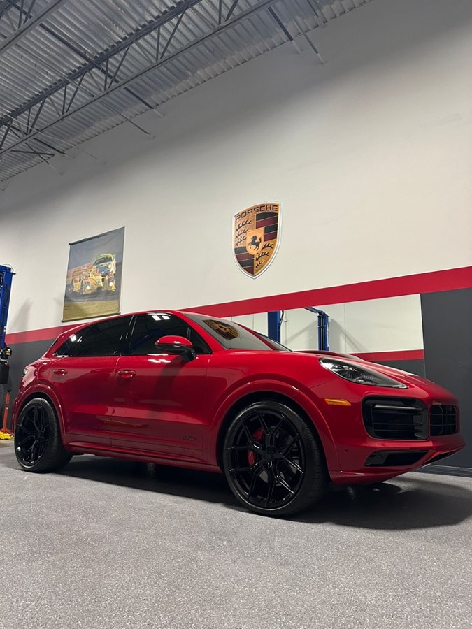 Red Cayenne GTS in front of the Porsche crest on the shop wall