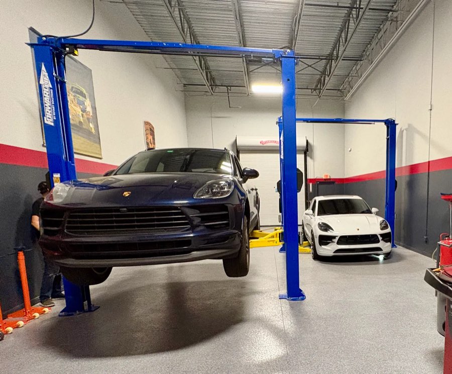 Blue Macan raised on a lift, with a white Macan in the next bay