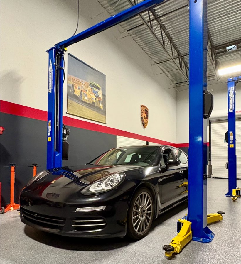 Black Panamera under a lift, beneath a painting of a Porsche race car