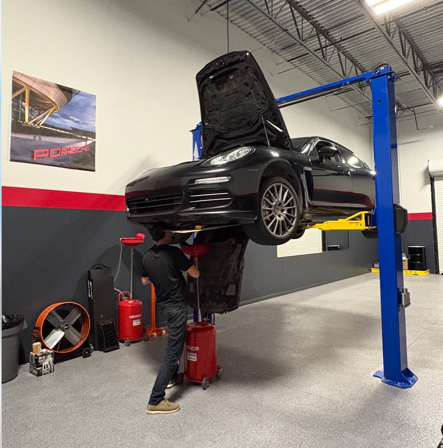 Black Panamera raised on a lift with its hood open while a technician drains the oil